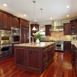 Kitchen in southwestern home with cherry wood cabinetry, large island, granite countertops and backsplashes, stainless steel appliances including gas stove with stainless vent hood and hardwood flooring