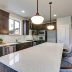 New kitchen boasts dark wood cabinets white backsplash subway tile and over sized island with white and grey quartz counter illuminated by pendant lights. We are a Silestone quartz countertop dealer.
